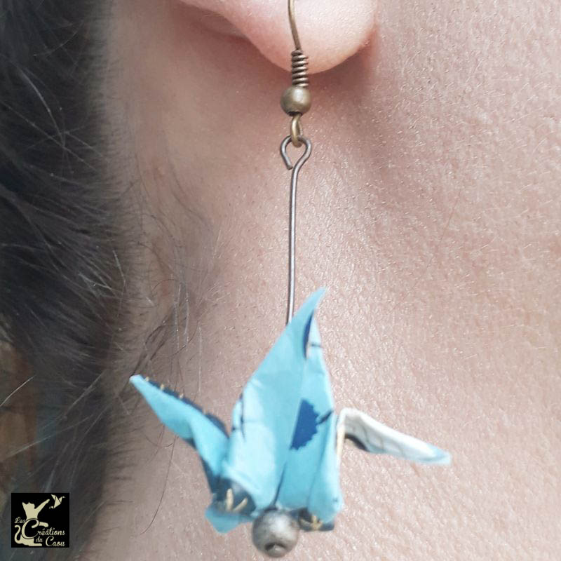 Boucles d'oreilles en origami. Le pliage est une grue traditionnelle réalisée à partir d'un papier japonais bleu ciel au motif fleuri bleu foncé et doré.