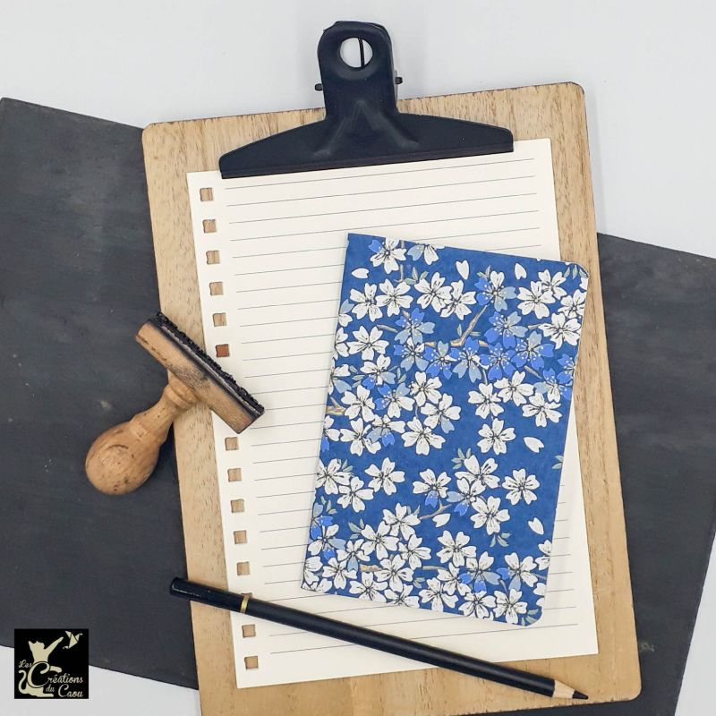 Carnet de notes au format A6. La couverture est recouverte à la main d’un papier japonais au fond bleu foncé orné de fleurs de sakura.