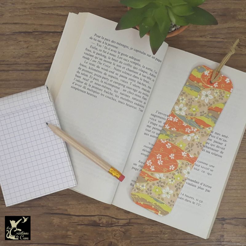 Ne perdez plus le fil de vos lectures ! Ce marque-page artisanal, recouvert d'un élégant papier japonais orné de fleurs sur fond orange, jaune, beige et gris clairdeviendra votre allié.