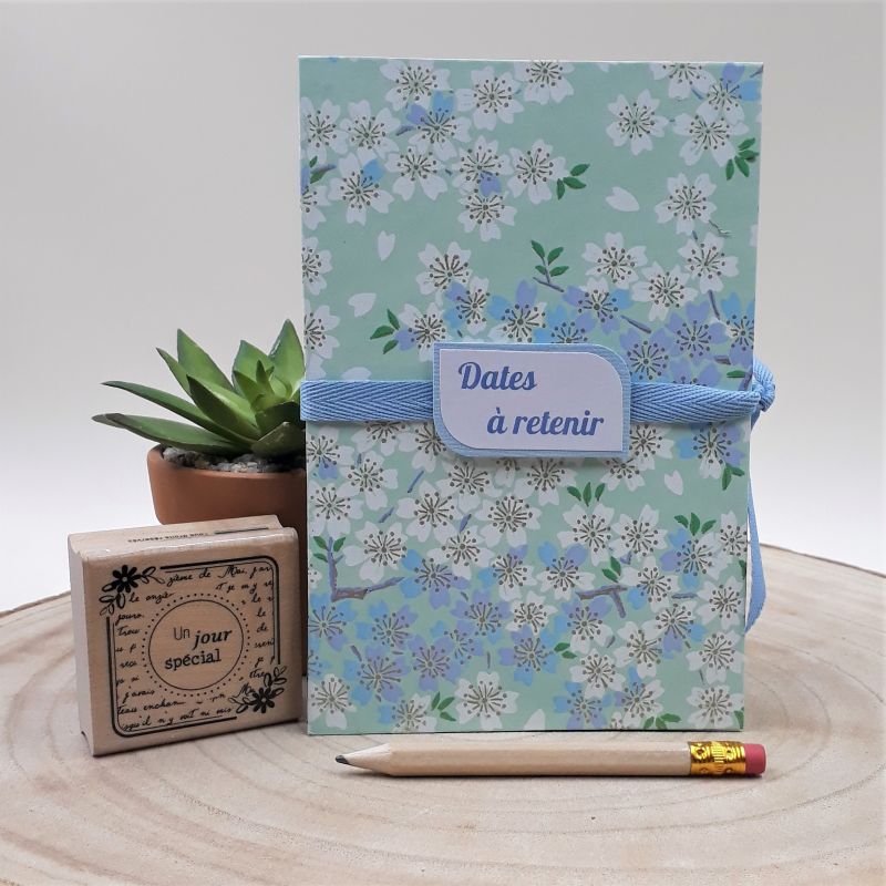 Calendrier des anniversaires recouvert d'un papier artisanal japonais vert d'eau au motif de fleurs de cerisiers blanches et bleues, entièrement réalisé à la main dans notre atelier de Lambersart (Lille).