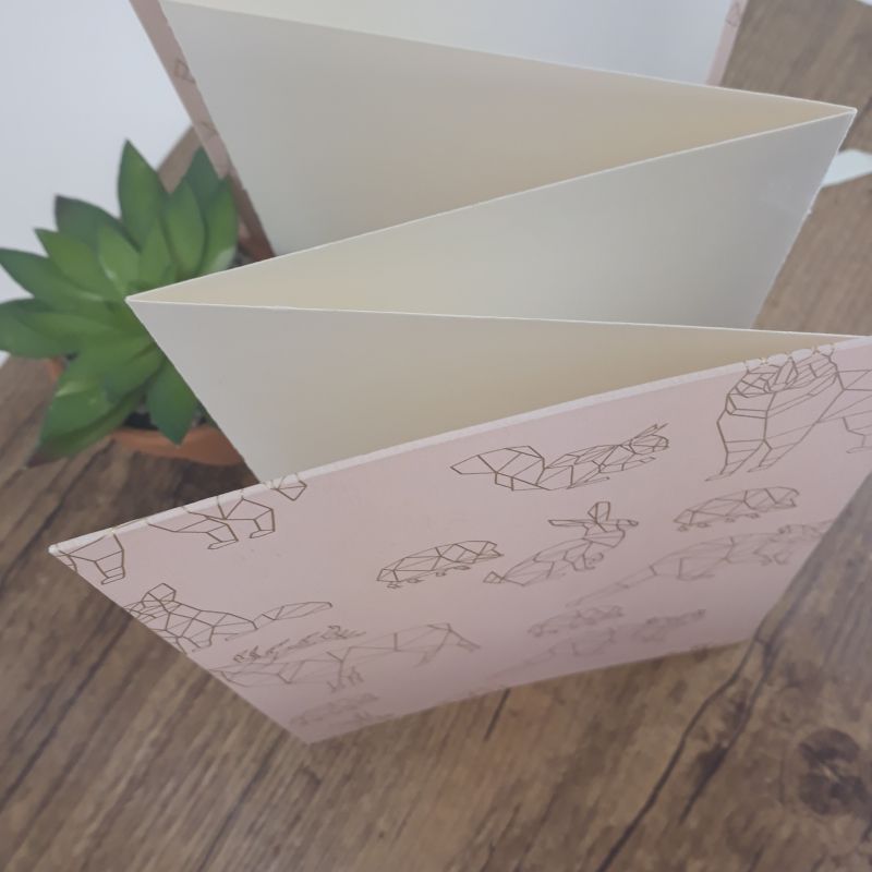 Album photo leporello réalisé à la main dans notre atelier de Lambersart (Lille), recouvert d'un papier italien rose tendre au motif d'animaux stylisés origami dorés.