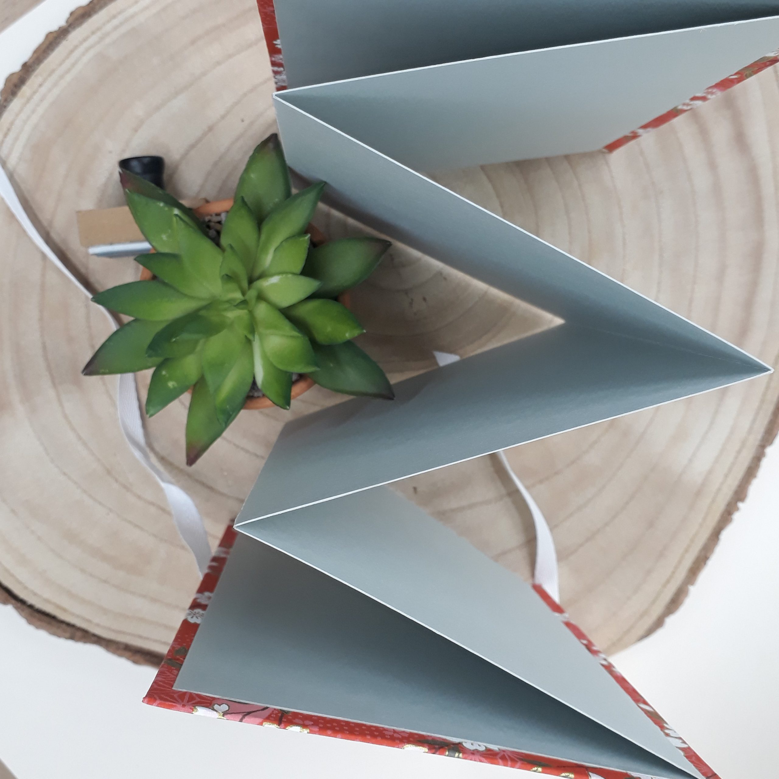 Album photo leporello réalisé à la main dans notre atelier de Lambersart (Lille), recouvert d'un papier japonais rouge au motif de fleurs de cerisiers (sakura) blanches.