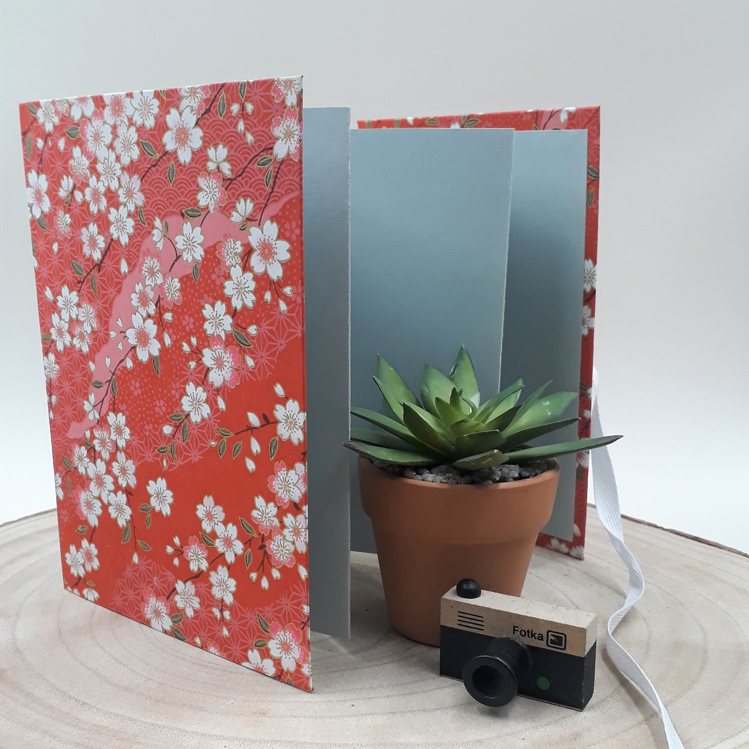 Album photo leporello réalisé à la main dans notre atelier de Lambersart (Lille), recouvert d'un papier japonais rouge au motif de fleurs de cerisiers (sakura) blanches.