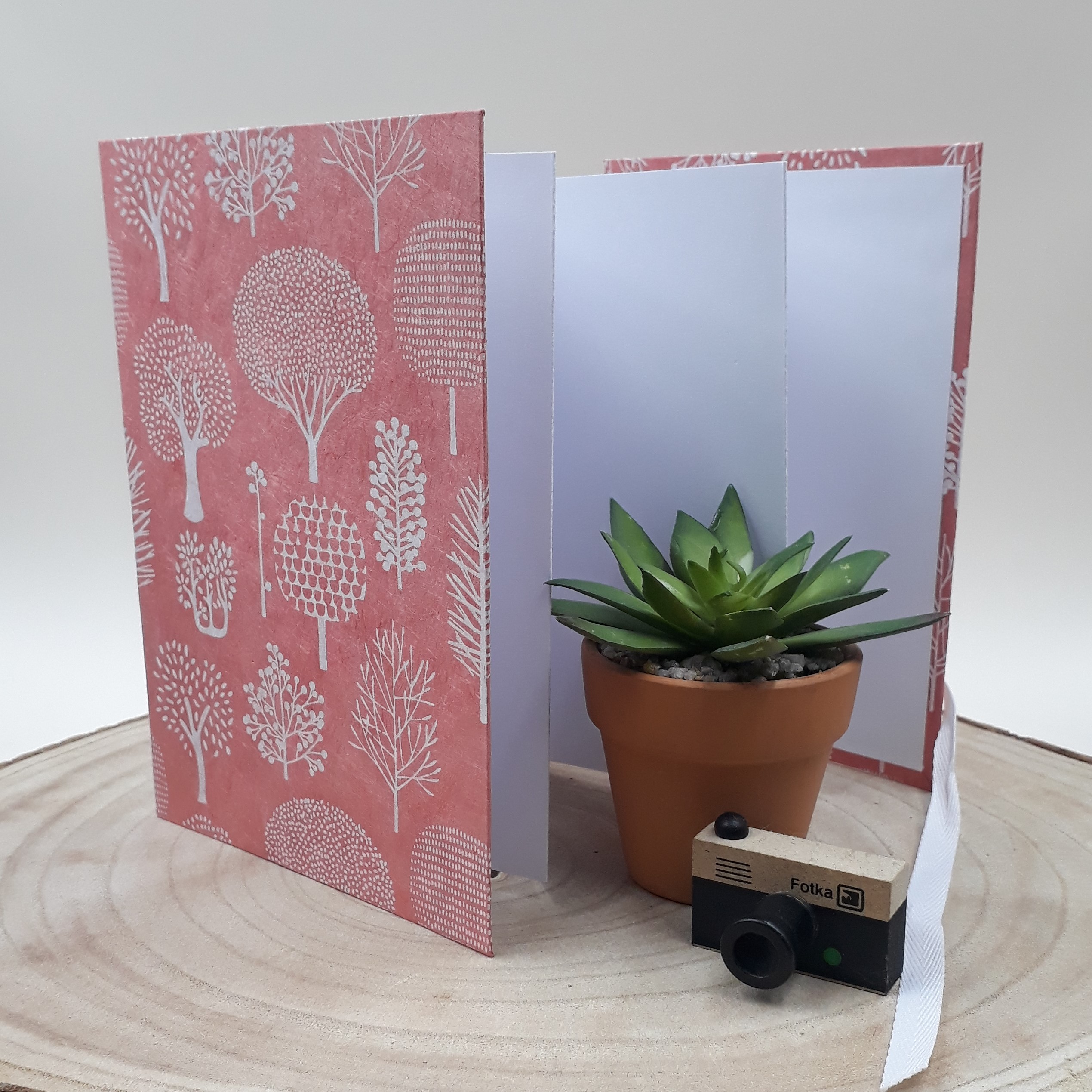 Album photo leporello réalisé à la main dans notre atelier de Lambersart (Lille), recouvert d'un papier népalais corail au motif d'arbres stylisés blancs.