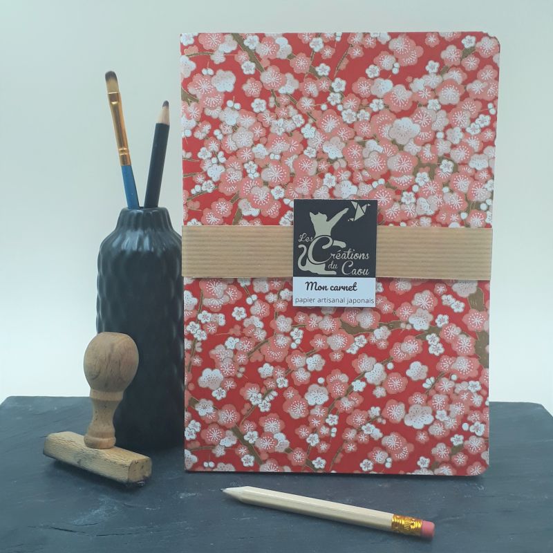 Carnet A5 recouvert à la main d'un papier artisanal japonais rouge orné de fleurs de pruniers rose et blanches.